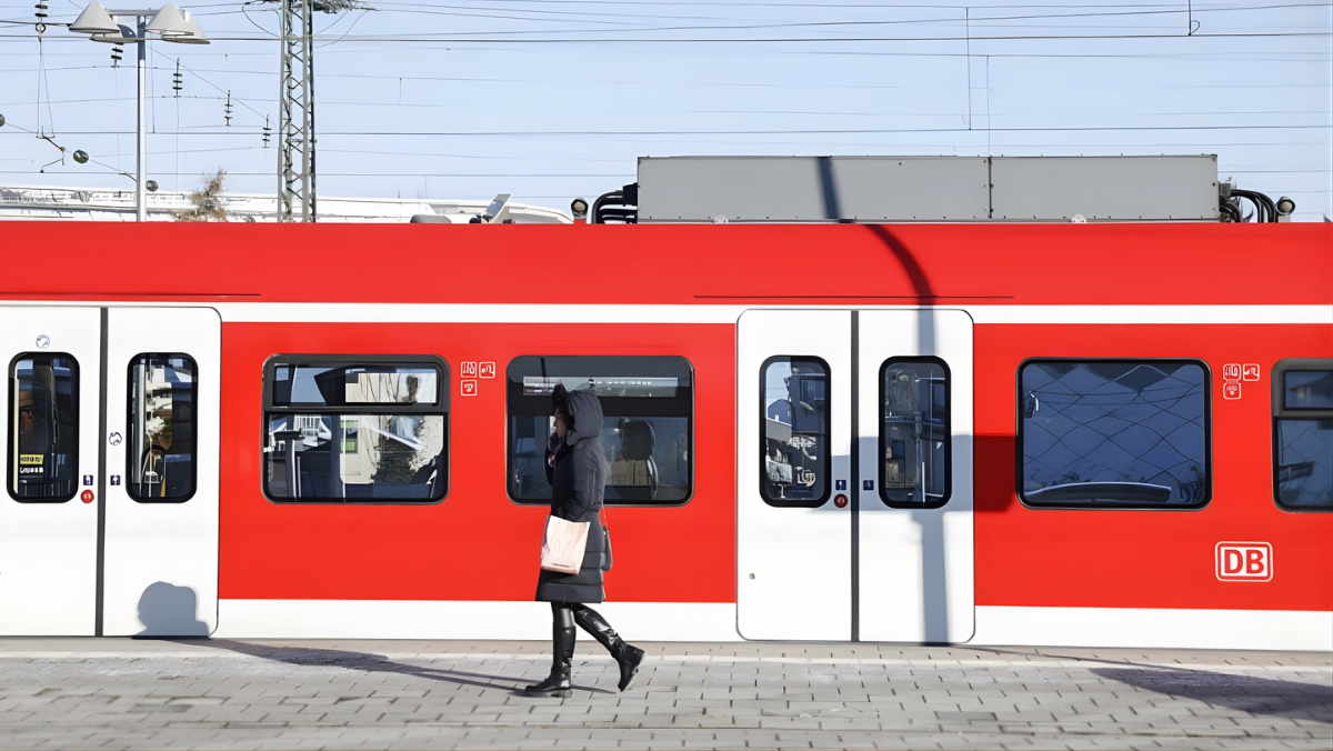 Person walking beside a red European commuter train at a station platform