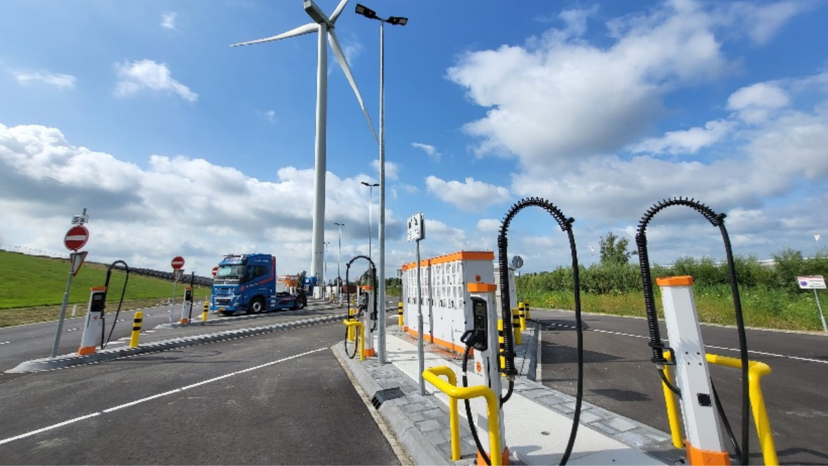 High-power EV charging station with multiple chargers beside a truck and wind turbine.