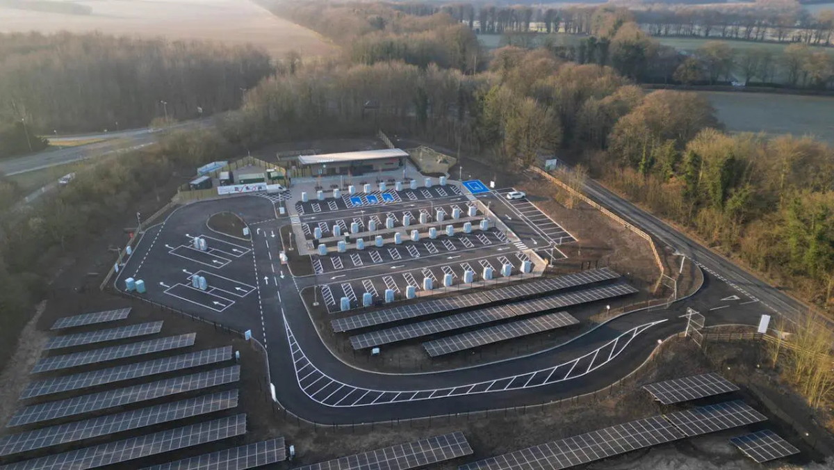 Aerial view of large EV charging hub with solar canopies and parking bays