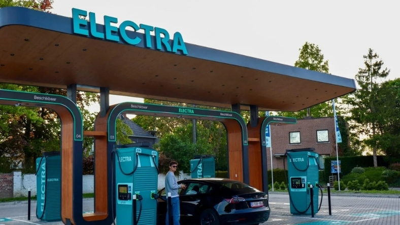 EV driver stands beside vehicle while charging at Electra public fast charging hub